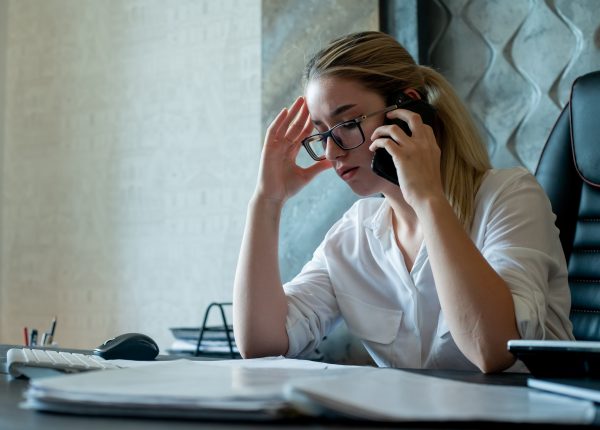 portrait of young office worker woman sitting at office desk with documents talking on mobile phone nervous and stressed working in office