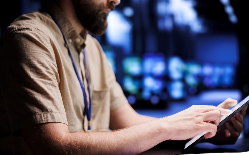 Electrician examining supercomputers Certified electrician using tablet to examine blade servers for power fluctuations. Licensed professional monitoring data center devices, identifying potential vulnerabilities, close up