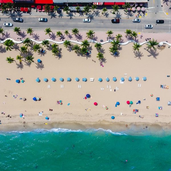 drone shot of beach with people,palm trees and blue umbrellas. Original public domain image from Wikimedia Commons